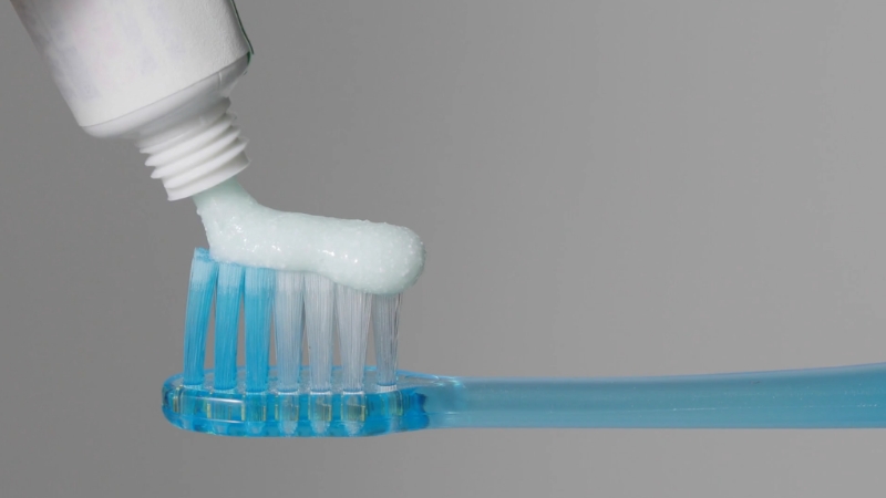 Toothpaste on a blue brush shows the risk tied to sharing a toothbrush
