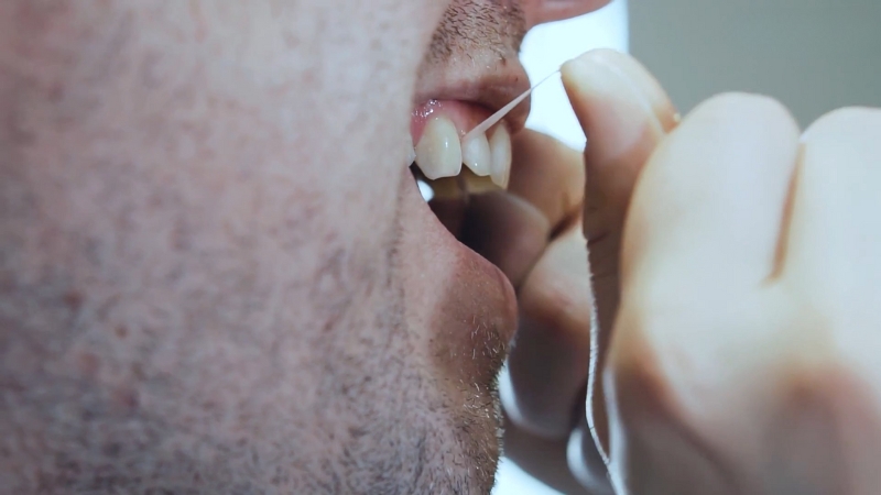 Man flosses between upper teeth to maintain oral hygiene