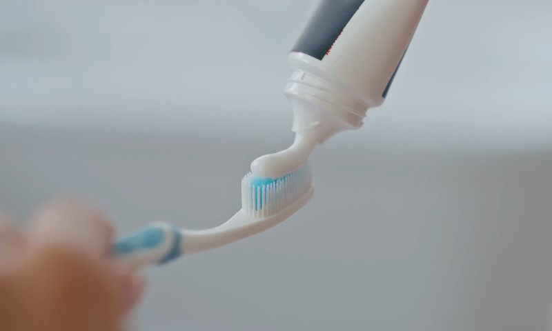 A person holds a toothbrush next to a tube of toothpaste