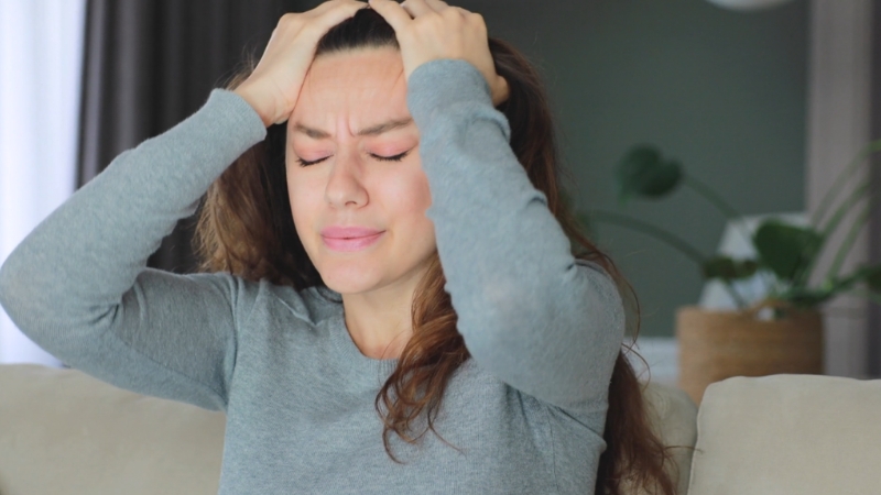 A woman holds her head in pain due to a strong headache after tooth extraction