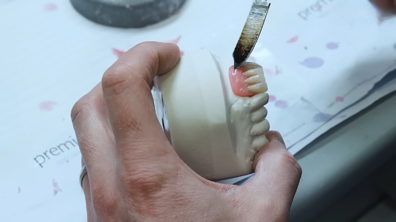 A close-up of a technician shaping the gum base on a partial denture model