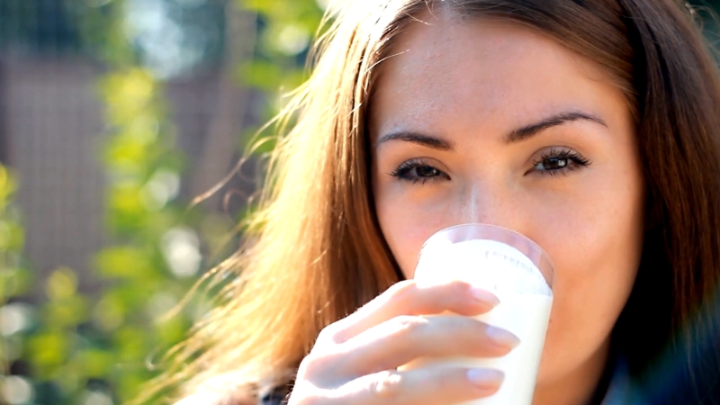 A woman drinks a glass of milk outdoors