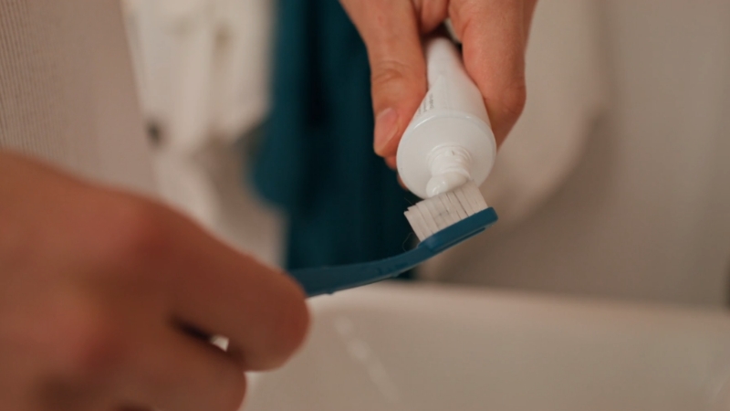 A person puts toothpaste on a blue brush to show basic toothbrush care