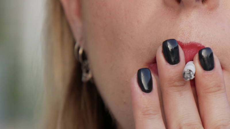 A woman smokes a cigarette close to her lips, showing a habit linked to smoking cause yellow teeth