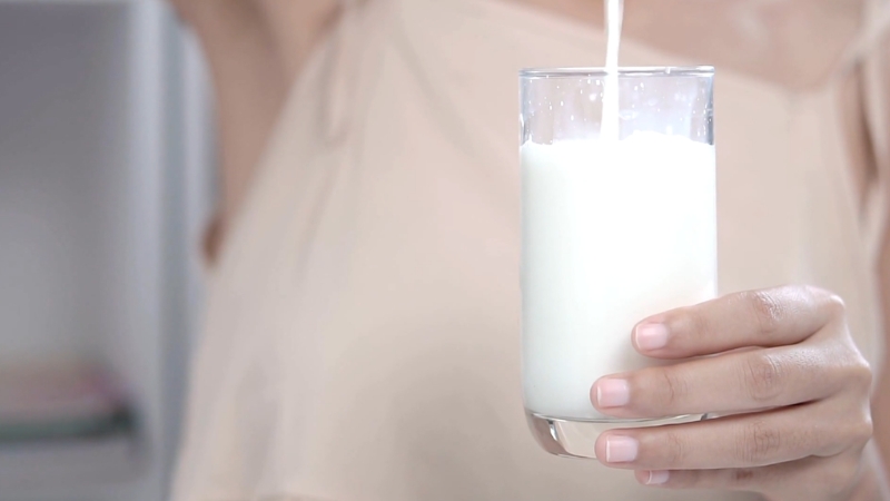 A hand holds a glass of milk as it is being poured