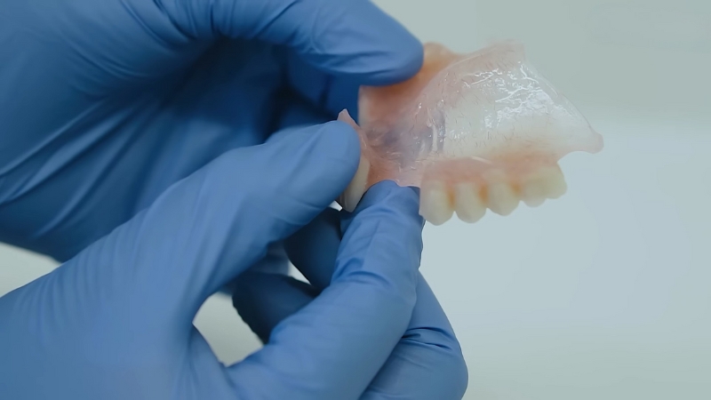 A gloved hand holding a flexible partial denture during a close-up examination