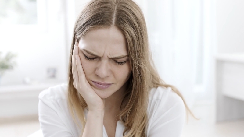 A woman shows clear wisdom tooth pain with her hand pressed to her jaw