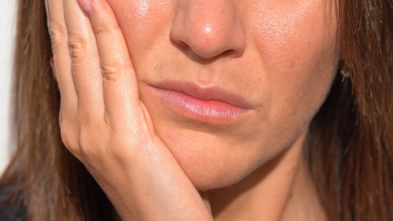 A woman holds her jaw in clear discomfort caused by wisdom tooth pain