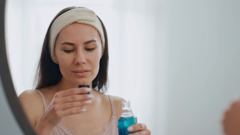 A woman prepares a small cup of blue mouthwash in front of a mirror
