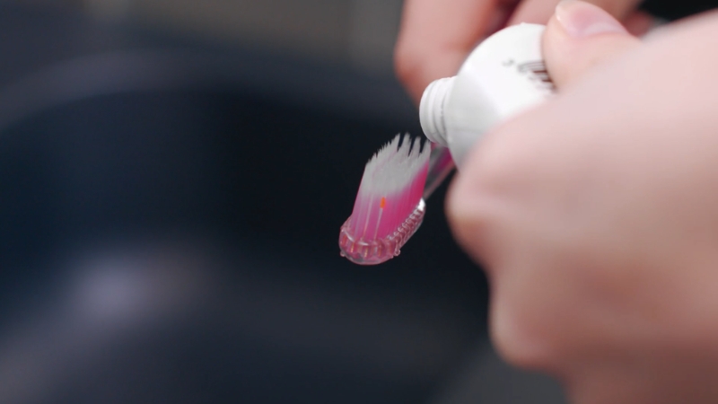 A person applies toothpaste onto a soft toothbrush before brushing