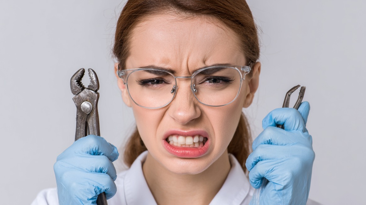 Woman in glasses and gloves holding dental extraction tools with a grimacing face